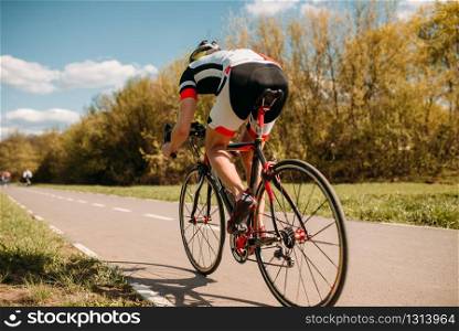 Cyclist in helmet and sportswear rides on bicycle, speed effect, back view. Workout on bike path, cycling. Cyclist rides on bicycle, speed effect