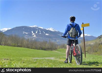 Cyclist in mountain bike near of sign on a path looking at the mountain