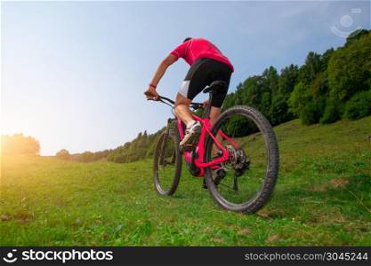 Cyclist man climbs a meadow with mountain bike.