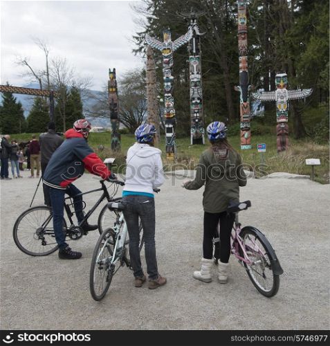 Cyclists viewing totem poles at Stanley Park, Vancouver, British Columbia, Canada