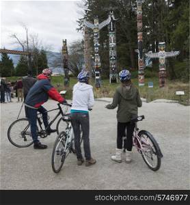 Cyclists viewing totem poles at Stanley Park, Vancouver, British Columbia, Canada