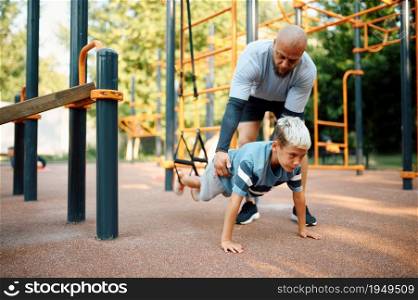 Dad and boy doing exercise with ropes, sport training on playground outdoors. The family leads a healthy lifestyle, fitness workout in summer park. Dad and boy doing exercise with ropes outdoors