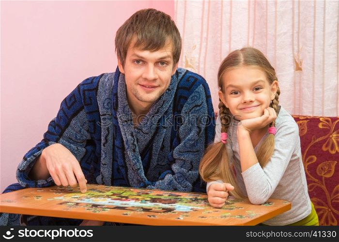 Dad and daughter in the frame looked sitting at the table and collecting puzzles