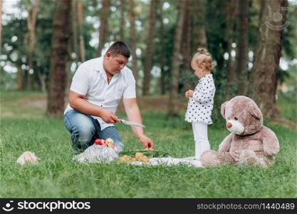 dad and little daughter on picnic in the park on summer day. Young father cuts watermelon. father&rsquo;s, baby&rsquo;s day. happy holiday. dad and little daughter on picnic in the park on summer day. Young father cuts watermelon. father&rsquo;s, baby&rsquo;s day. happy holiday.