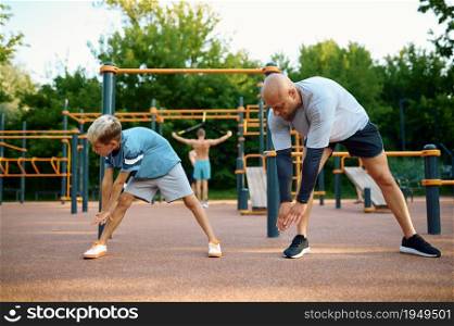 Dad and son doing exercise, sport training on playground outdoors. The family leads a healthy lifestyle, fitness workout in summer park. Dad and son doing exercise, sport training