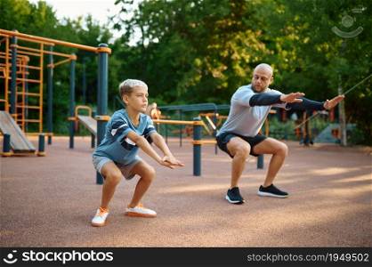 Dad and son doing exercise, sport training on playground outdoors. The family leads a healthy lifestyle, fitness workout in summer park. Dad and son doing exercise, sport training
