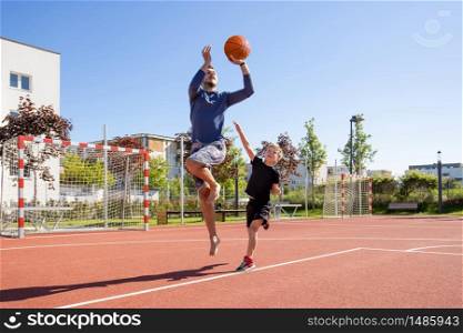 Dad and son playing basketball barefoot with the ball on a playground