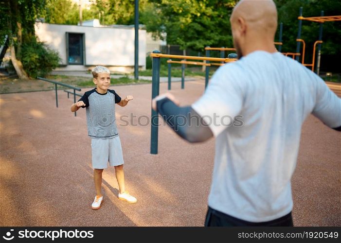Dad and son, sport training on playground outdoors. The family leads a healthy lifestyle, fitness workout in summer park. Dad and son, sport training on playground