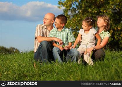 dad, mom, son and daughter in early fall park. they sitting on grass and looking at sunset