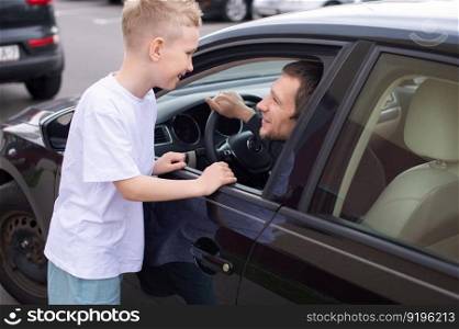Dad smiles at his son, the child meets the father, a black car, a meeting in the city. to come home, to say goodbye near the car, to see off to work, a boy in a white T-shirt, his father&rsquo;s smile, an open window. Dad came home in a black car. Son meets Father