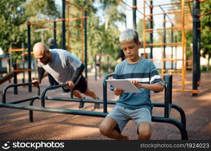Daddy and boy on exercise machine, sport training on playground outdoors. The family leads a healthy lifestyle, fitness workout in summer park. Daddy and boy on exercise machine, sport training