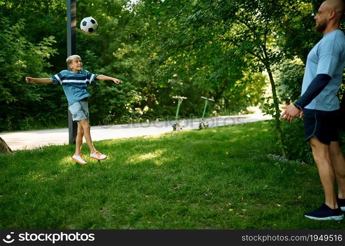 Daddy and boy play football on the grass outdoors. The family leads a healthy lifestyle, morning fitness workout in summer park. Daddy and boy play football on the grass in park