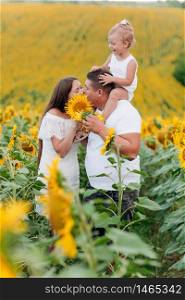 Daddy&rsquo;s carrying a baby daughter on his shoulders in the field of sunflowers. The concept of summer holiday. Father&rsquo;s, mother&rsquo;s, baby&rsquo;s day. Spending time together. Family look. Couple kissing. Daddy&rsquo;s carrying a baby daughter on his shoulders in the field of sunflowers. The concept of summer holiday. Father&rsquo;s, mother&rsquo;s, baby&rsquo;s day. Spending time together. Family look. Couple kissing.