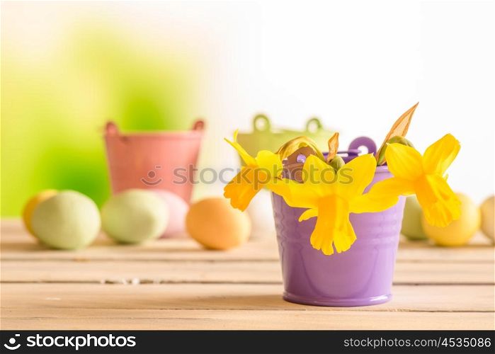 Daffodils in a purple flowerpot with easter eggs in the background
