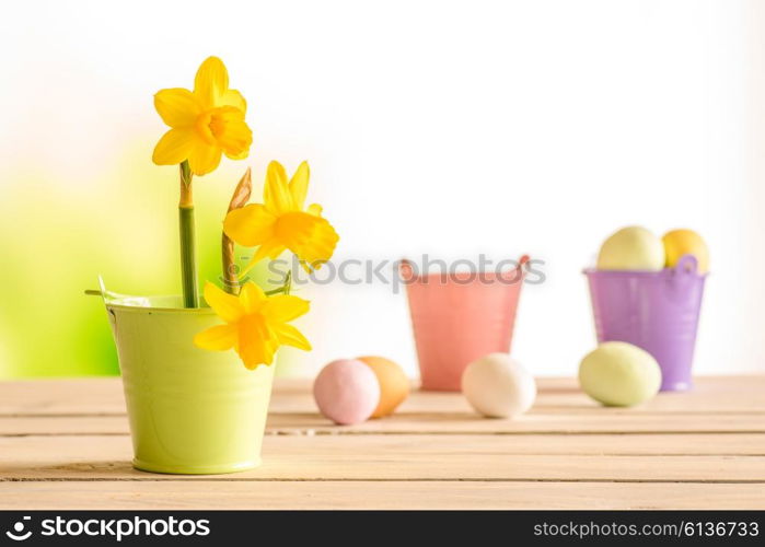 Daffodils in the easter on a wooden table with easter eggs in the background