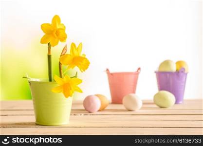 Daffodils in the easter on a wooden table with easter eggs in the background