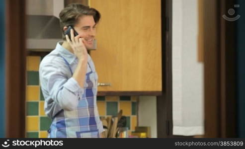 Daily chores: young husband cutting vegetables and cooking in kitchen at home while talking on the phone