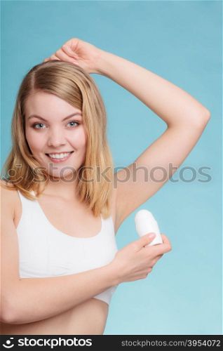 Daily skin care and hygiene. Girl applying stick deodorant in armpit. Young woman putting antiperspirant in underarms on blue