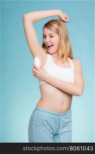 Daily skin care and hygiene. Girl applying stick deodorant in armpit. Young woman putting antiperspirant in underarms on blue
