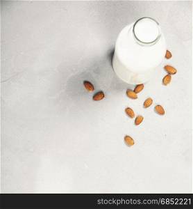 Dairy alternative milk. Almond milk in bottle and fresh nuts over grey background, top view, selective focus, copy space. Clean eating, dairy-free, vegan, detox, allergy-friendly, healthy food concept
