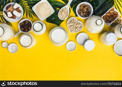 Dairy free milk substitute drinks and ingredients on yellow background, flat lay. Vegan, vegetarian, clean eating concept