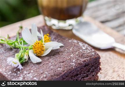 Daisy Flower on Chocolate Brownie Cake with Latte Coffee and Spoon on Wood Table Left Close Up. Relax coffee break time in coffee shop left frame