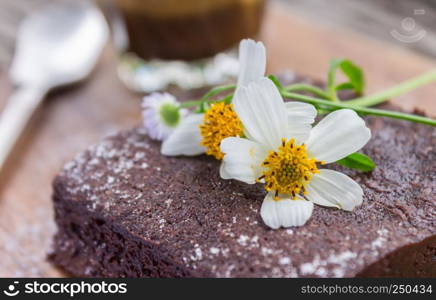 Daisy Flower on Chocolate Brownie Cake with Latte Coffee and Spoon on Chopping Board or Cutting Board on Wood Table Right Close Up. Relax coffee break time in coffee shop right frame