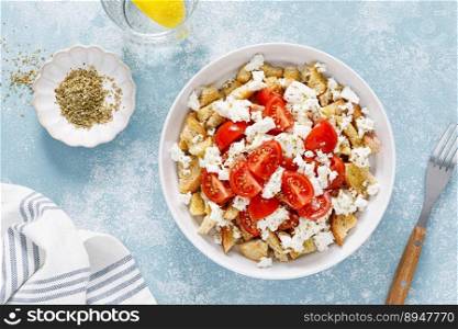 Dakos or koukouvagia salad. Classic recipe Cretan barley rusk salad with fresh tomato, mizithra cheese and oregano. Traditional mediterranean Greek cuisine. Healthy food, diet. Top view