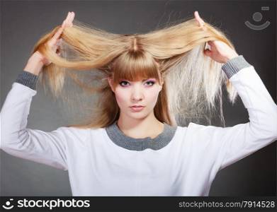 Damaged dry woman hair. Closeup woman holding hands long hair and looking unhappy on gray background.