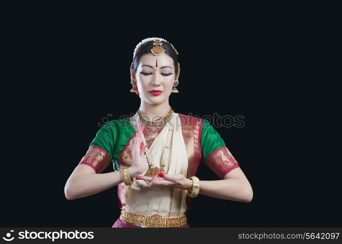 Dancer with eyes closed performing Bharatanatyam against black background