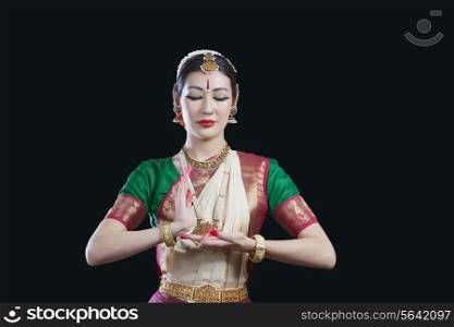 Dancer with eyes closed performing Bharatanatyam against black background