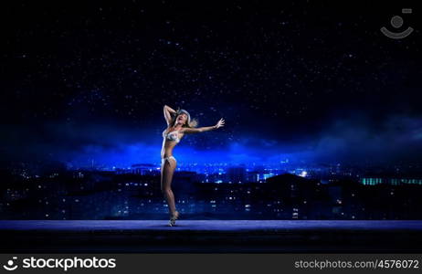 Dancing blonde in bikini. Hot young dancing woman in white bikini on dark background