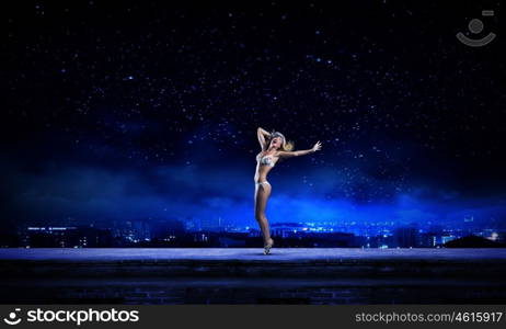 Dancing blonde in bikini. Hot young dancing woman in white bikini on dark background