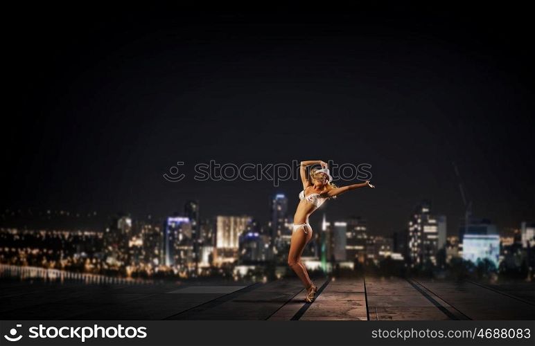 Dancing blonde in bikini. Hot young dancing woman in white bikini on dark background