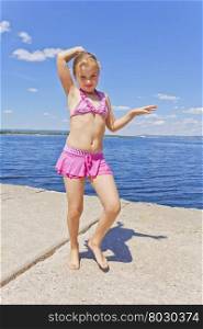Dancing girl in pink swimsuit on the riverbank