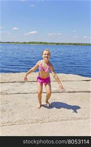 Dancing girl on the riverbank in pink swimsuit