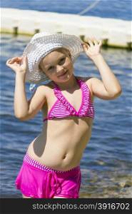 Dancing girl on the riverbank in pink swimsuit and white hat