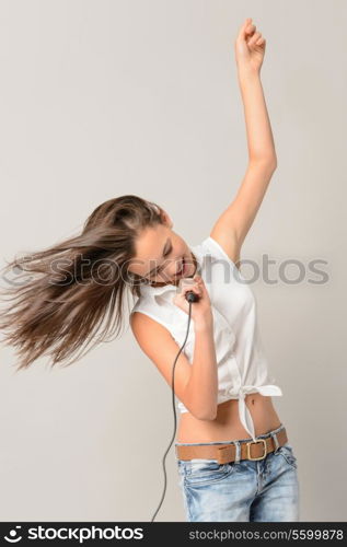 Dancing teenage girl singing with microphone blowing hair on gray background