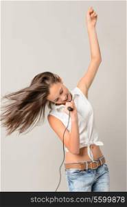 Dancing teenage girl singing with microphone blowing hair on gray background