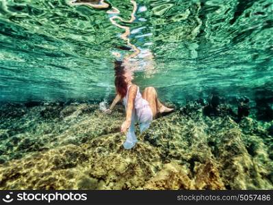 Dancing underwater, beautiful young female swimming in the sea near beautiful coral garden, active lifestyle, summer holidays and vacation concept