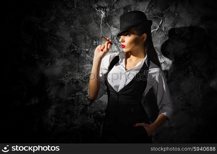 Dangerous and beautiful criminal girl with cigar on grey wall