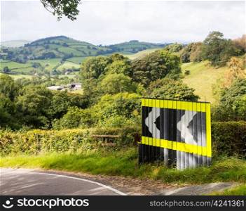 Dangerous bend in road with arrow signs in rolling countryside of Wales