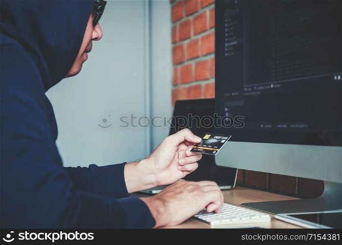 Dangerous Hooded Hacker using credit card typing bad data into computer online system and spreading to global stolen personal information. Cyber security concept