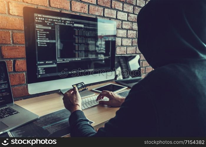Dangerous Hooded Hacker using credit card typing bad data into computer online system and spreading to global stolen personal information. Cyber security concept
