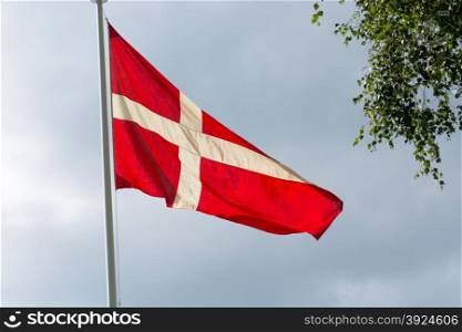 Danish flag. Danish flag on a flag pole in summer with gray clouds in the background