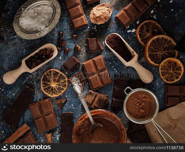 Dark and milk chocolate bars with dry orange slices, cinnamon sticks and coffee beans on blue background