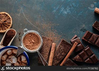 Dark and milk chocolate bars with dry orange slices, cinnamon sticks and coffee beans on blue background. Copyspace.