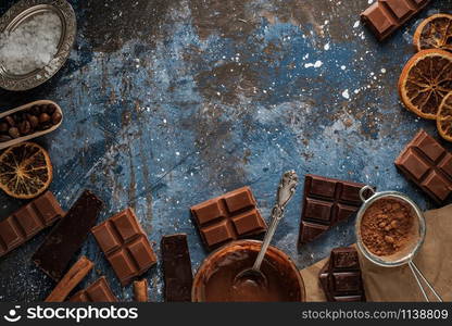 Dark and milk chocolate bars with dry orange slices, cinnamon sticks and coffee beans on blue background. Copyspace.