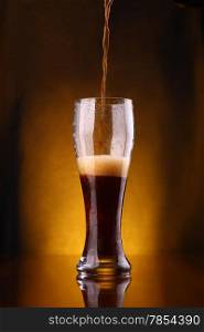 Dark beer pouring into a tall glass from a bottle