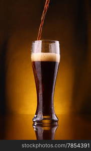 Dark beer pouring into a tall glass from a bottle